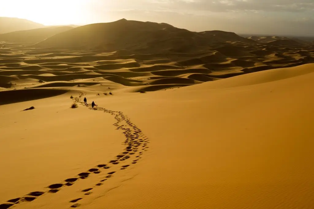 two people climbing sahara dunes under the sun